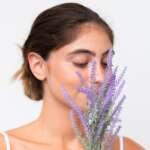 Young pretty caucasian woman isolated on white background holding a lavender plant close up portrait. Health Benefits of Lavender concept