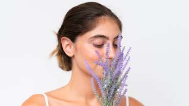 Young pretty caucasian woman isolated on white background holding a lavender plant close up portrait. Health Benefits of Lavender concept