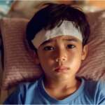 Febrile seizures in a child concept. A boy resting in bed with cooling gel patch on forehead, suffering from a fever
