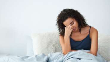 Adult woman is sick, sitting on her bed representing causes of iron deficiency anemia concept