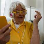 A cheerful woman listening to music in the kitchen. gadgets for seniors concept