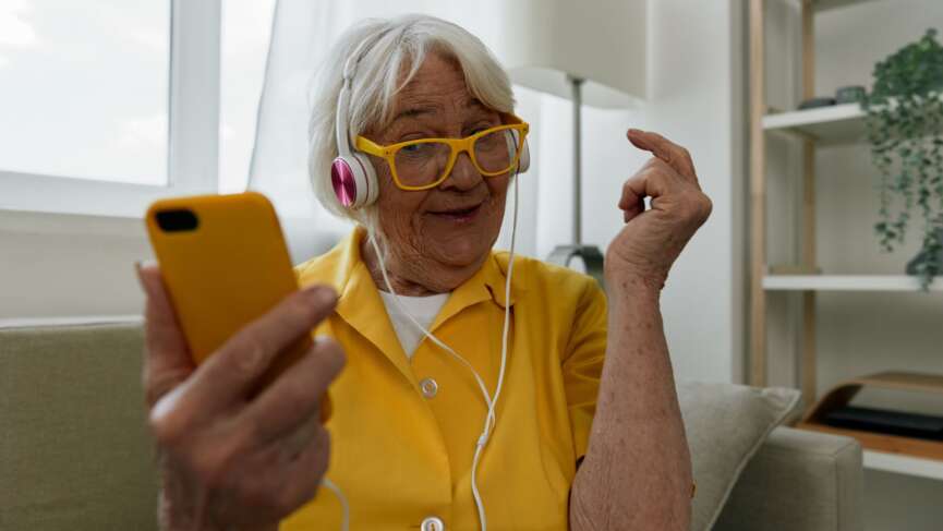 A cheerful woman listening to music in the kitchen. gadgets for seniors concept