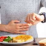 A person is looking at his watch, and there is a plate full of nutritional veggies. health benefits of fasting concept