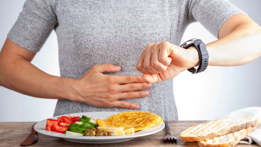 A person is looking at his watch, and there is a plate full of nutritional veggies. health benefits of fasting concept