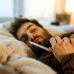 A sick man is lying on the sofa checking his temperature. Fever in adults concept