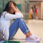 depressed girl sitting with backpack in school corridor with depression in students concept