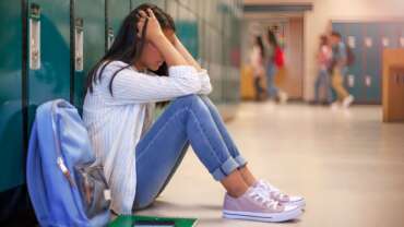 depressed girl sitting with backpack in school corridor with depression in students concept