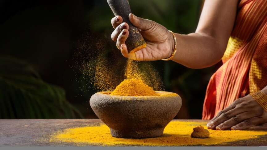 Indian spice turmeric powder splashing from a stone mortar in closeup. health benefits of turmeric concept