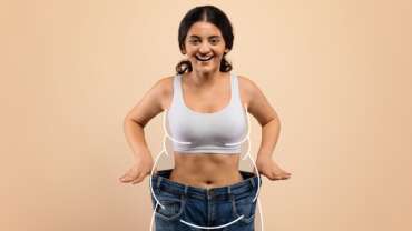 A beautiful young woman with black hair holding her jeans of a much bigger size. facts about weight loss concept