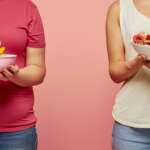One girl is holding a bowl full of carbs while the other is full of protein. carbs vs. protein concept