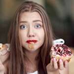 A young blonde girl eating delicious colorful donuts. warning signs of sugar concept