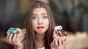 A young blonde girl eating delicious colorful donuts. warning signs of sugar concept