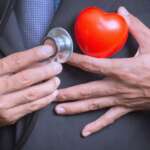 A doctor holding her hand on her chest with a stethoscope and heart model, representing common misconceptions of heart health