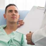 A senior man consulting with a doctor sitting on a hospital bed