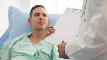 A senior man consulting with a doctor sitting on a hospital bed