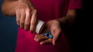 man pouring painkillers pills from bottle into hand
