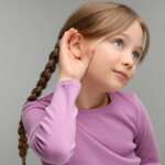 Little girl with hand near ear with hearing loss problem concept