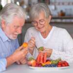 a cheerful senior couple enjoying a healthy breakfast at home with a variety of nutritious foods, representing the concept of top foods to eat after age 50 for healthy aging