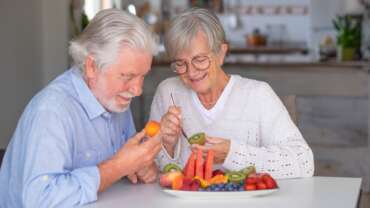 a cheerful senior couple enjoying a healthy breakfast at home with a variety of nutritious foods, representing the concept of top foods to eat after age 50 for healthy aging
