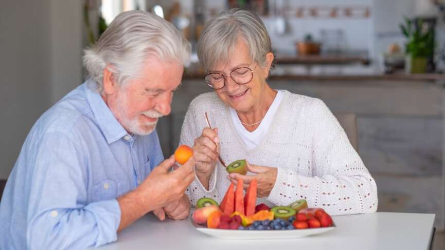a cheerful senior couple enjoying a healthy breakfast at home with a variety of nutritious foods, representing the concept of top foods to eat after age 50 for healthy aging